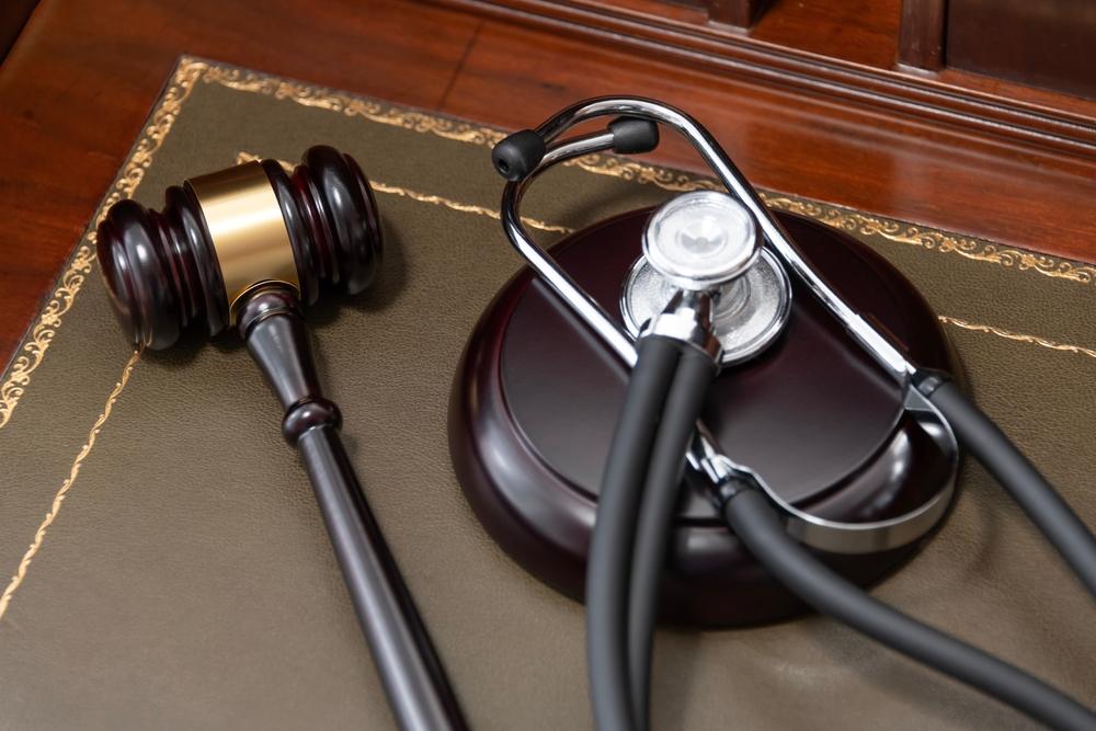 A close-up of a judge's gavel and a black stethoscope on top of a legal book, signifying the intersection of law and medicine.
