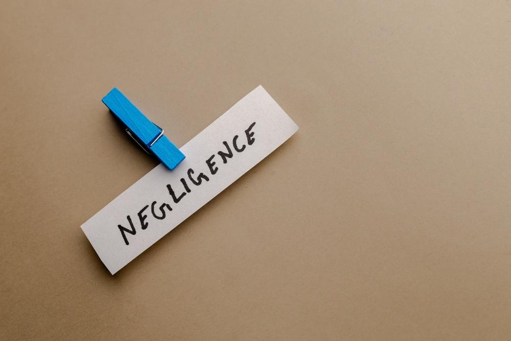 This conceptual studio shot features the word negligence handwritten on a white paper strip secured by a bright blue clothespin against a clean neutral background for corporate theme use